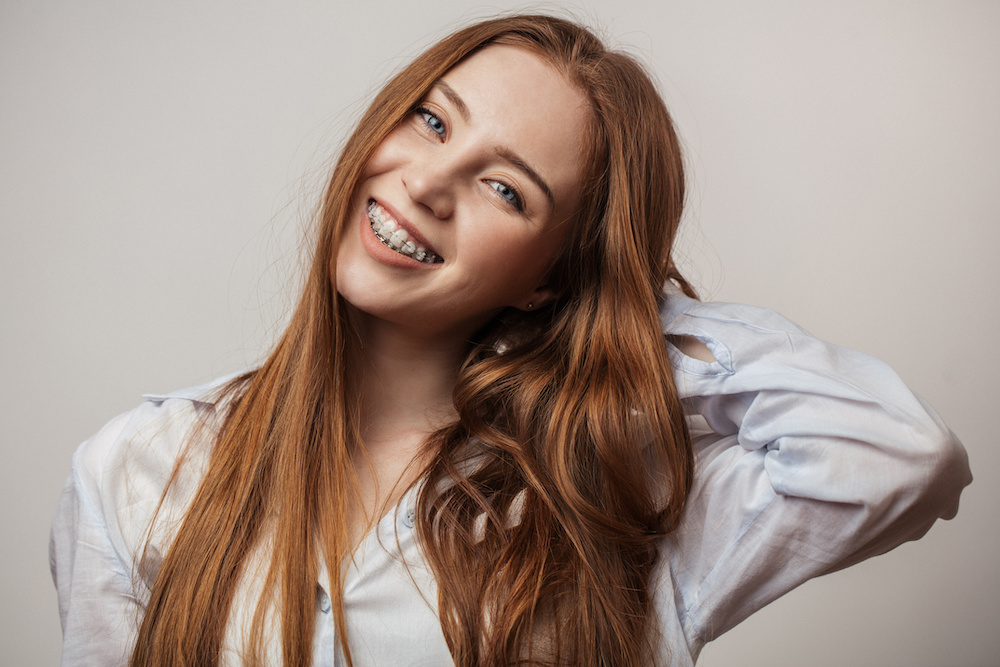 Happy young red-haired woman in braces smiling on white background looking at camera